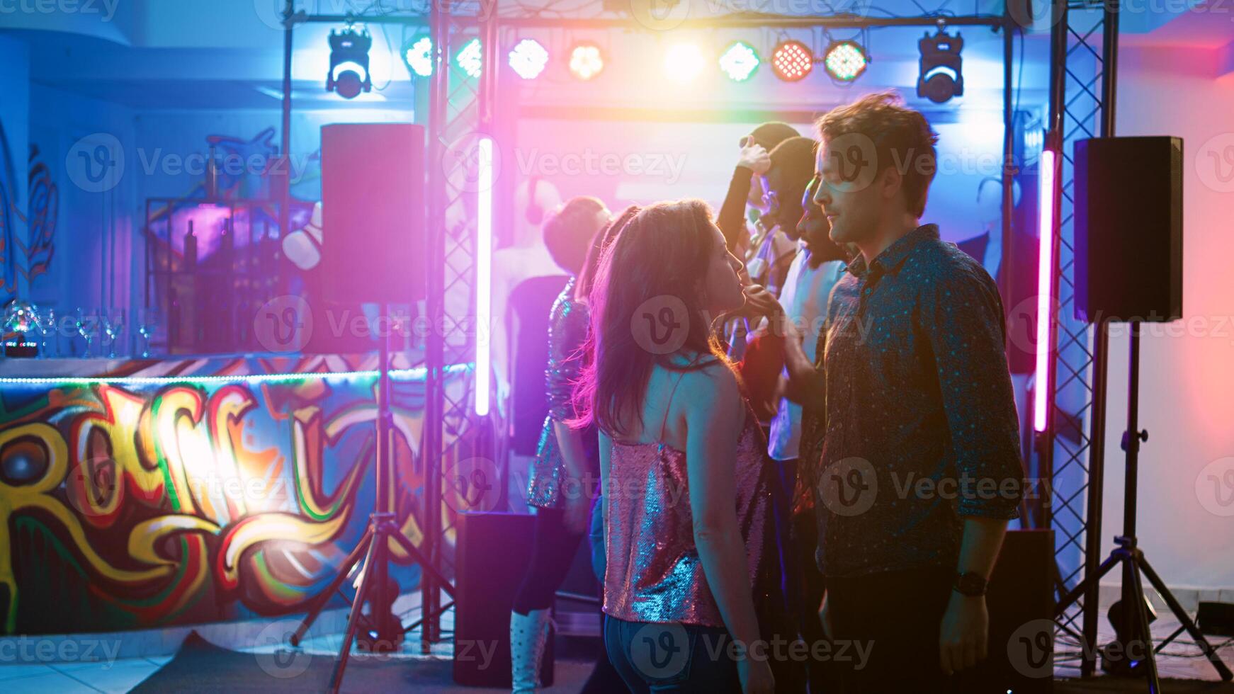 Men and women dancing at funky party with electronic music, having fun with cool dance battle at social gathering. Young friends partying on club dance floor, show off. Handheld shot. photo