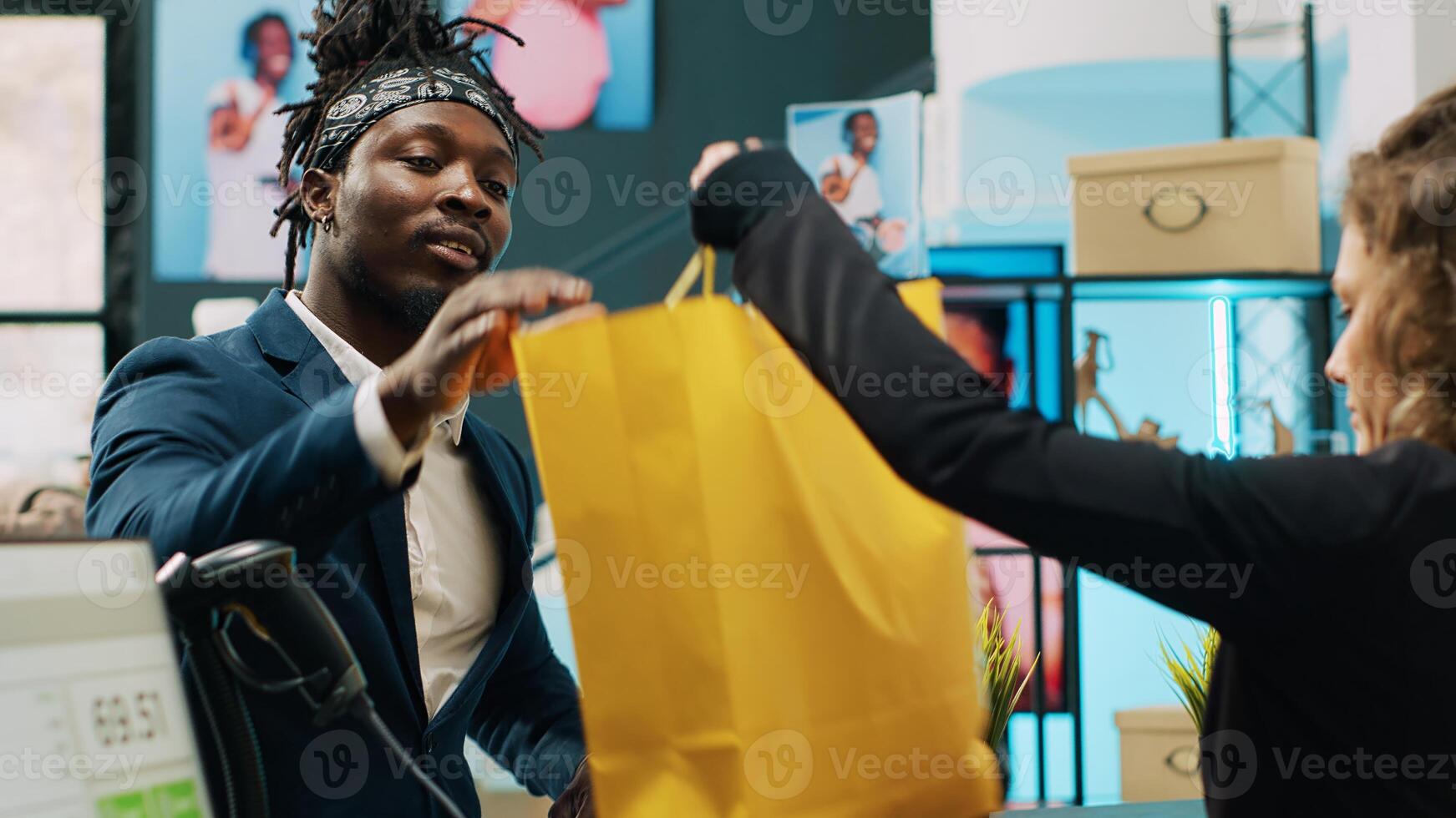 africano americano cliente pago con tarjeta a pos en ropa almacenar, compras para traje chaquetas y formal elementos. empleado trabajando a efectivo registro, Rico cliente haciendo pago a verificar. cámara una. foto