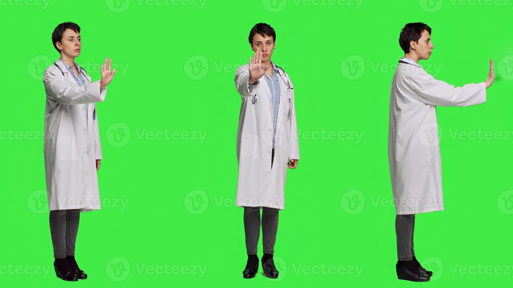 Woman physician raising palm and doing stop sign in studio, expressing rejection and denial against greenscreen backdrop. General practitioner showing warning symbol with negative reaction. Camera A. photo