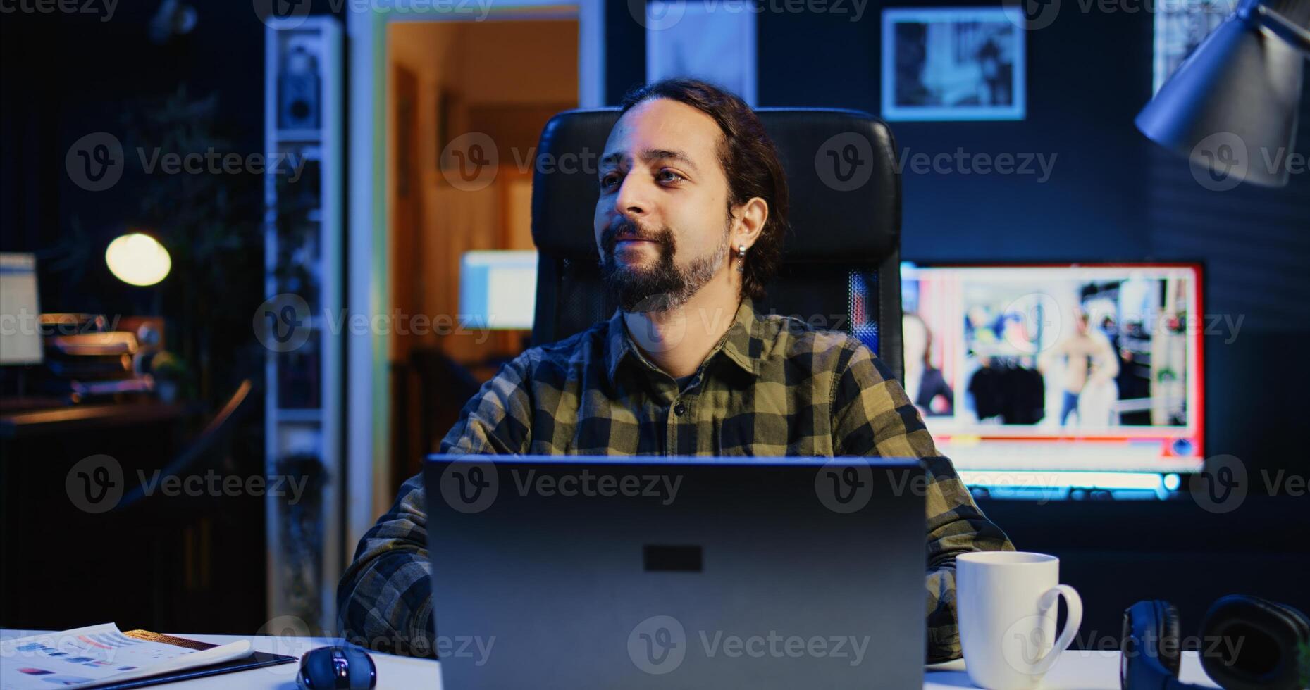 Portrait of happy man sitting at home office desk, preparing to solve tasks on laptop. Cheerful freelancer in front of digital device, doing email communication in living room, camera B photo