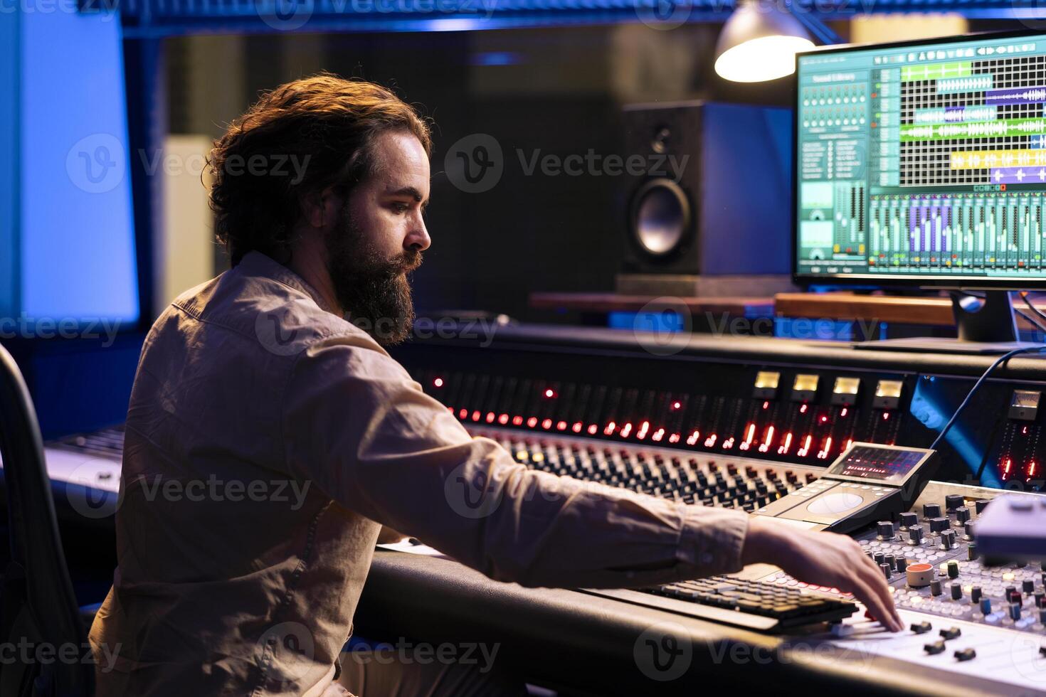 Portrait of music producer working in control room with sliders and switchers, adjusting volume level on audio recordings. Audio engineer works with mixing console in professional studio. photo