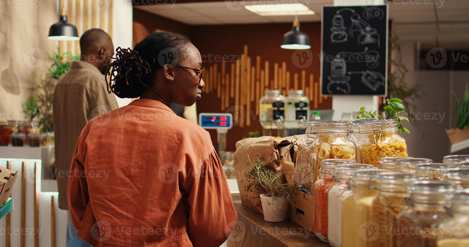 African american client examines bio homemade bulk products, looking to buy natural ethically sourced food alternatives for healthy nutrition. Woman shopping for goods at zero waste store. Camera 2. photo