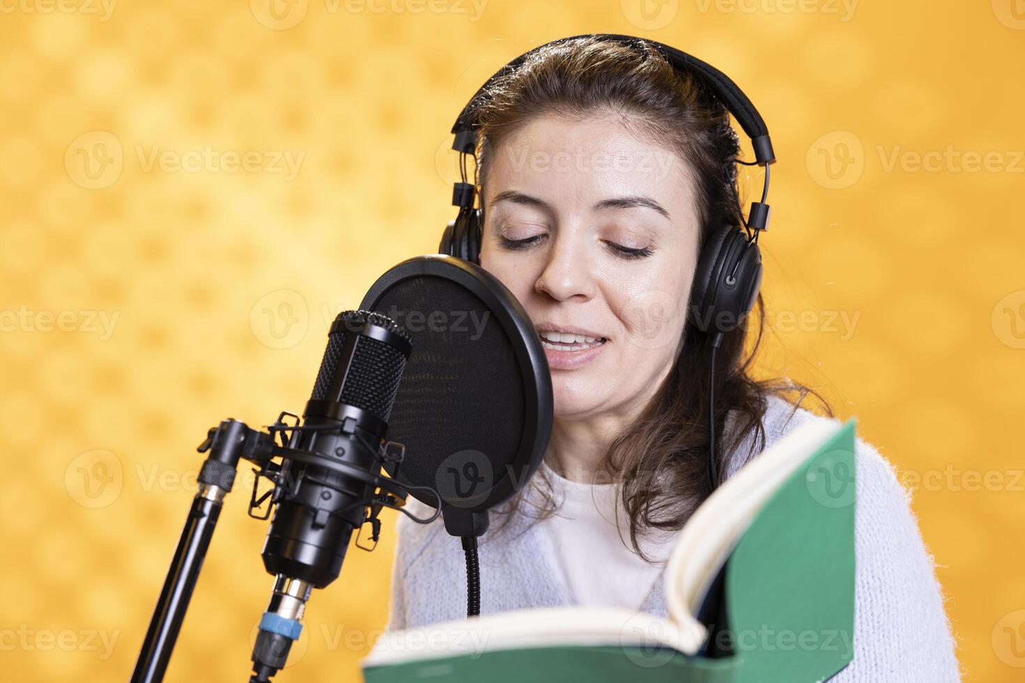 Smiling lady doing voiceover reading of book to produce audiobook. Happy voice actor using storytelling skills to entertain audience while producing digital recording of novel, studio background photo