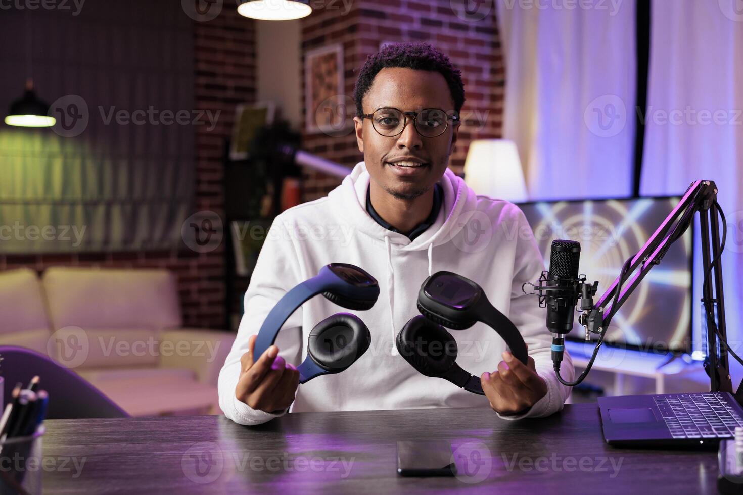 Portrait of technology reviewer recording headphones comparison episode using professional microphone in living room studio. Experienced content creator filming audiophiles channel vlog photo