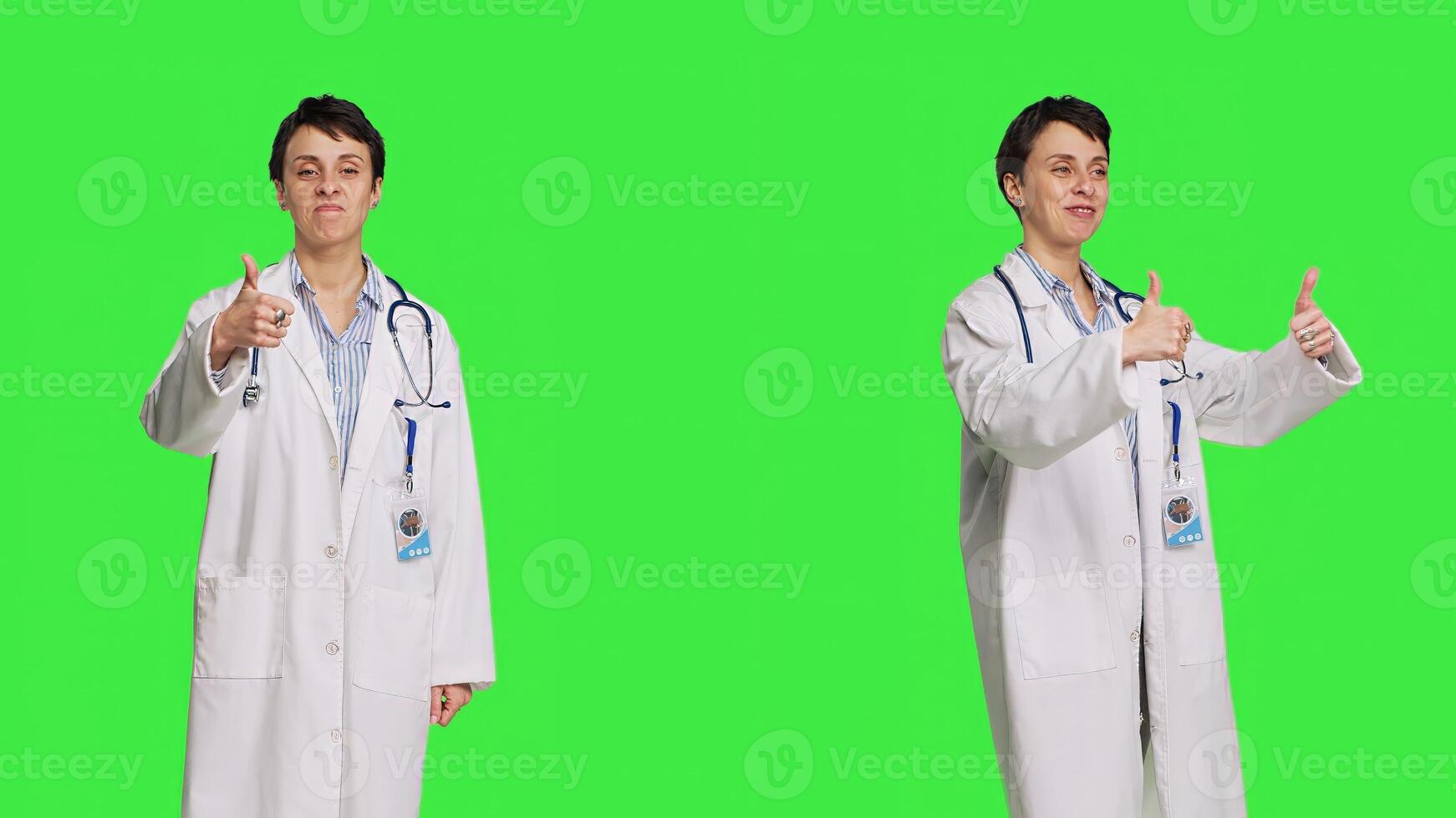 Cheerful medic doing thumbs up symbol against greenscreen backdrop, expresses positivity with like sign. General practitioner with coat giving approval and being satisfied with success. Camera B. photo