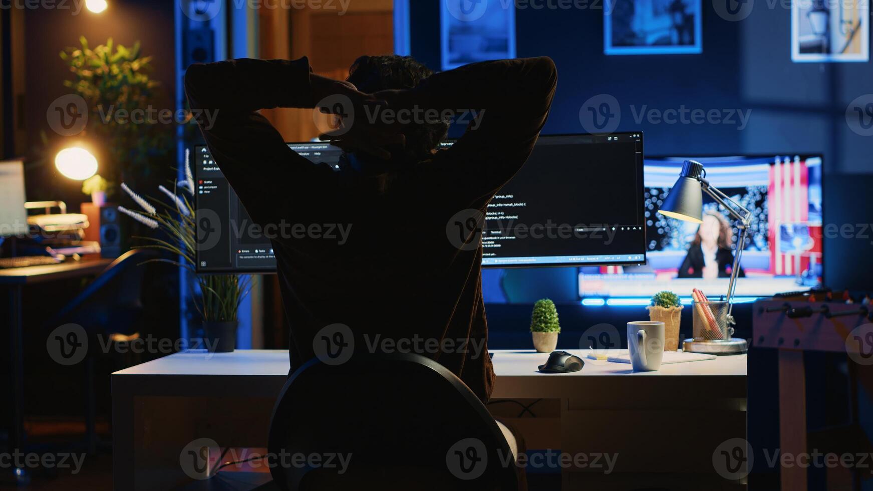 Man doing IT support job from home office, stretching after sitting on desk chair all day. Programmer loosening up, relaxing after typing on computer for long period of time, camera A photo