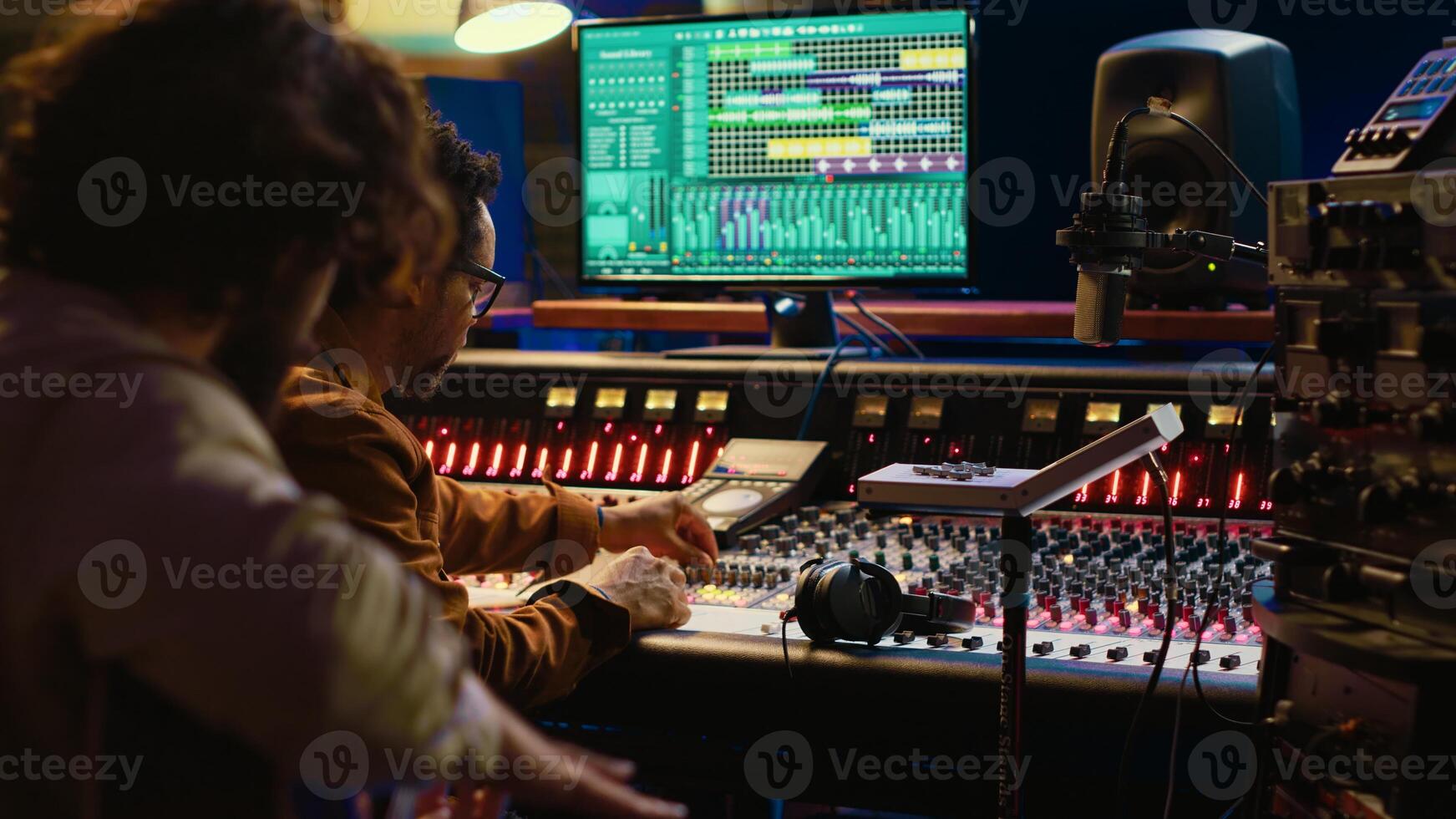 Guitarist recording his electro acoustic instrument and song in studio, producing new music with a sound engineer in control room. Skilled musician songwriter recording tracks. Camera A. photo