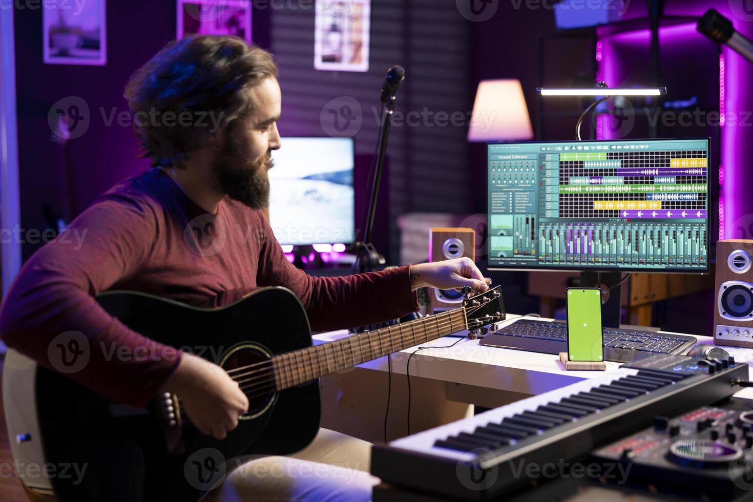 Musician learning to tune his guitar with internet tutorial via greenscreen on phone, twisting the knobs and practicing music lessons. Artist songwriter does rehearsal with acoustic instrument. photo