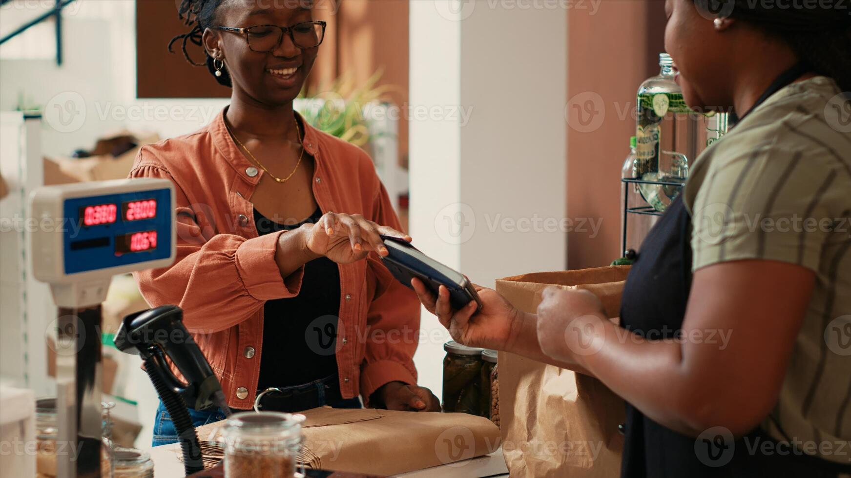 African american client paying for bio goods at checkout, buying freshly harvested ethically sourced produce from local farmers market. Buyer using card at pos terminal, eco friendly. photo