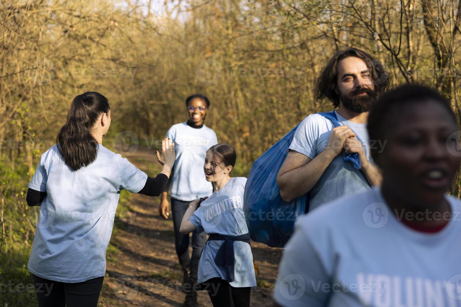 Motivated happy group of people sharing high five with her friends, finishing litter cleanup of the forest and saving the nature. Satisfied activists congratulating and praising each other. photo