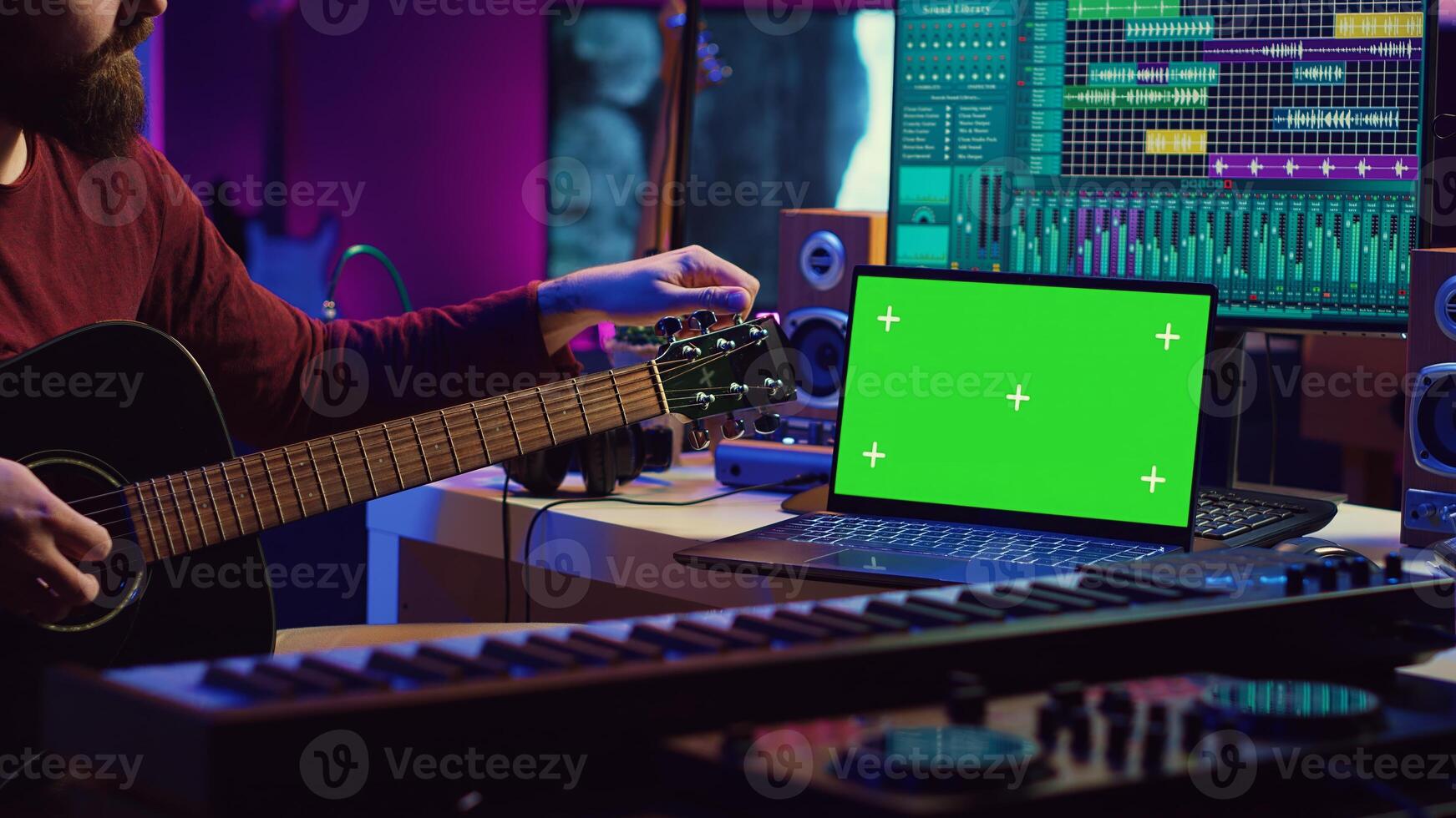 Musician learning to play new acoustic instrument in his home studio, practicing online guitar lessons on isolated greenscreen display. Watching tutorial on laptop to develop his skills. Camera A. photo