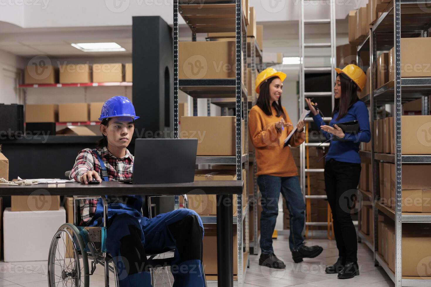 Warehouse worker in wheelchair planning delivery on laptop in logistics and distribution center storage room. Young asian storehouse employee with disability analyzing clients orders checklist photo