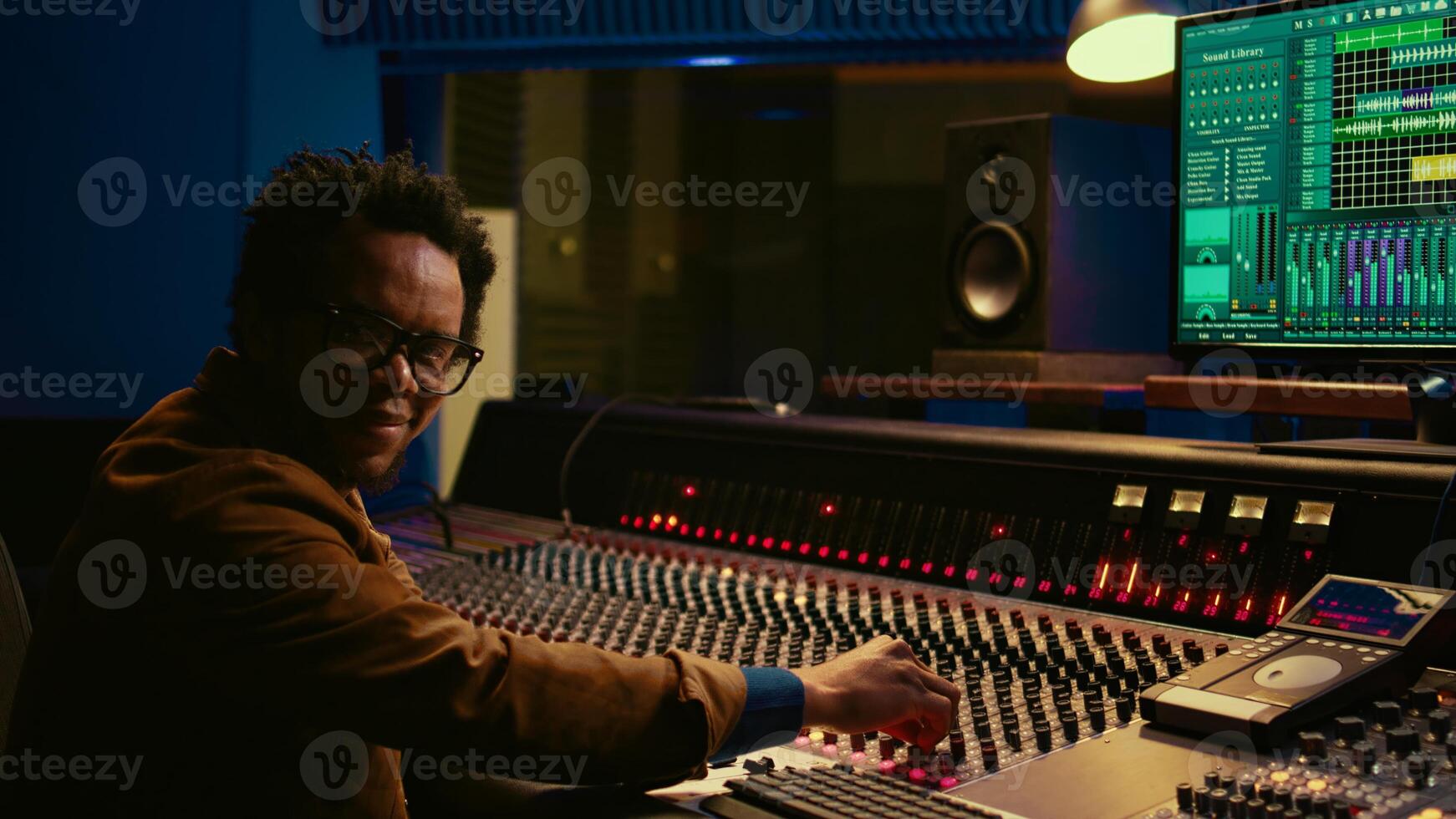 retrato de africano americano sonido diseñador mezcla y dominar pistas con profesional audio consola en estudio controlar habitación. productor técnico usos caja de resonancia almohadillas en mezclador estación. cámara b. foto