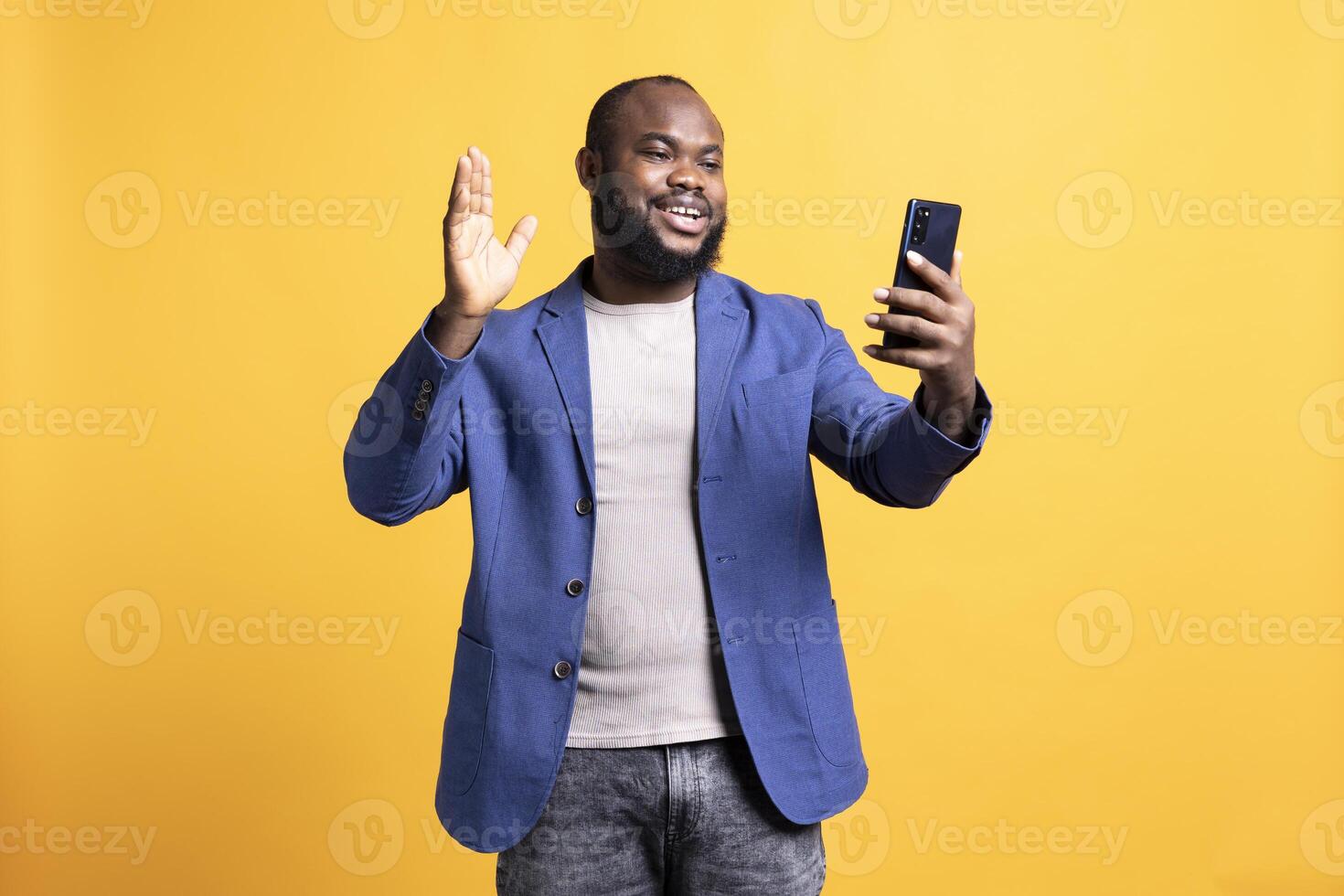 Smiling man having friendly conversation with friends during teleconference meeting using smartphone, studio background. BIPOC person having fun catching up with mates during online call photo