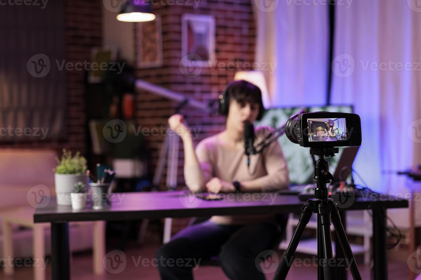 Focus shot on modern camera recording vlogger in blurry background talking about personal development subjects. Entertaining woman speaking on air during online show in studio photo