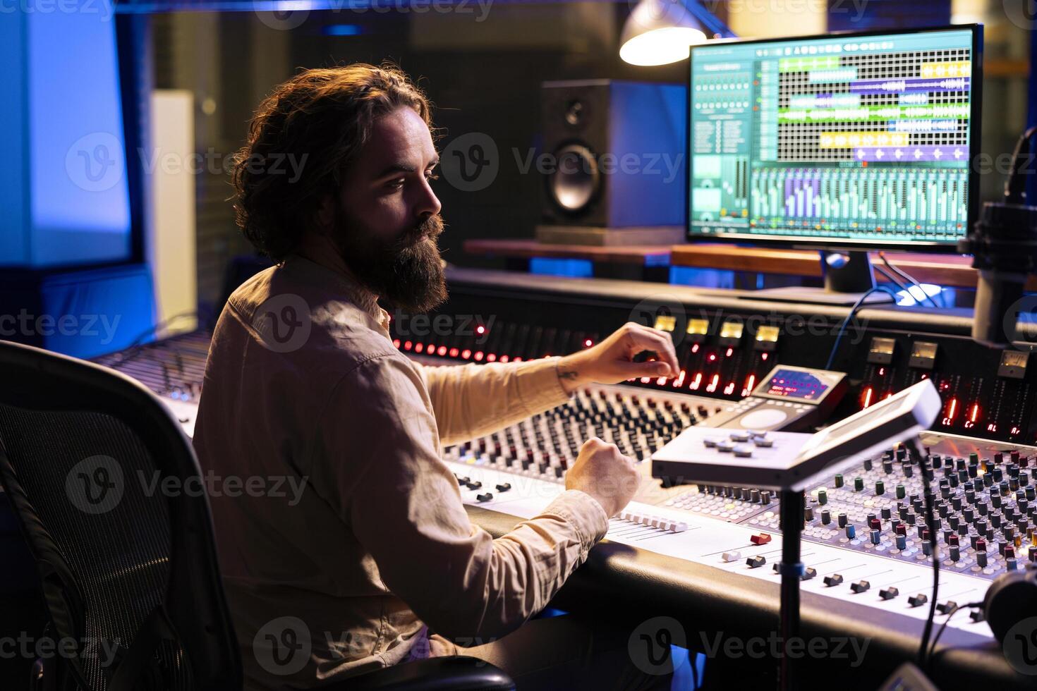 Music technician mixing and mastering songs with motorized faders and knobs, using control desk dashboard and computer. Young sound engineer creating tracks for an album in studio. photo