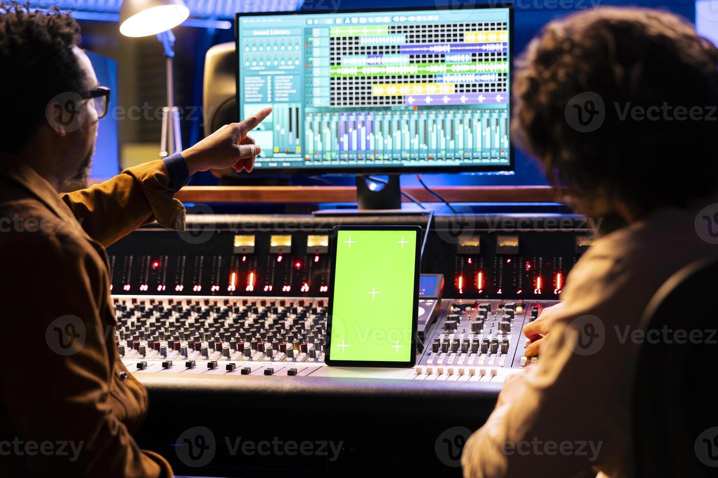 Artist and sound engineer working with greenscreen display on tablet, mixing and mastering tracks with audio console and digital software. Musicians team editing music, motorized faders. photo