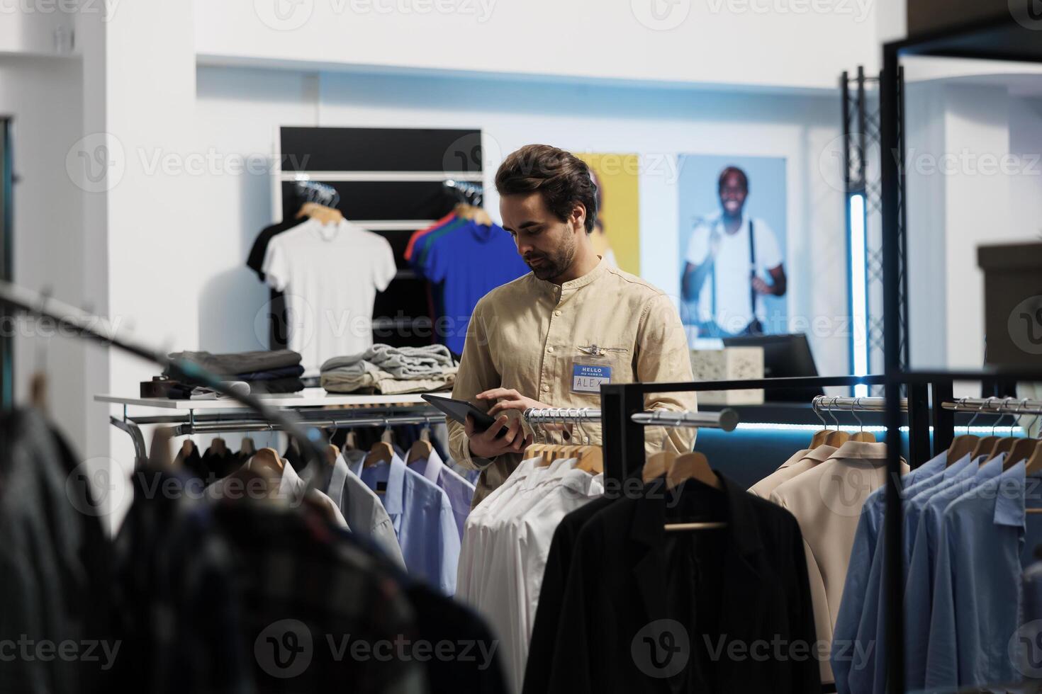 Clothing store caucasian man employee checking garment stock availability on digital tablet. Shopping center fashion outlet manager updating merchandise information on website photo