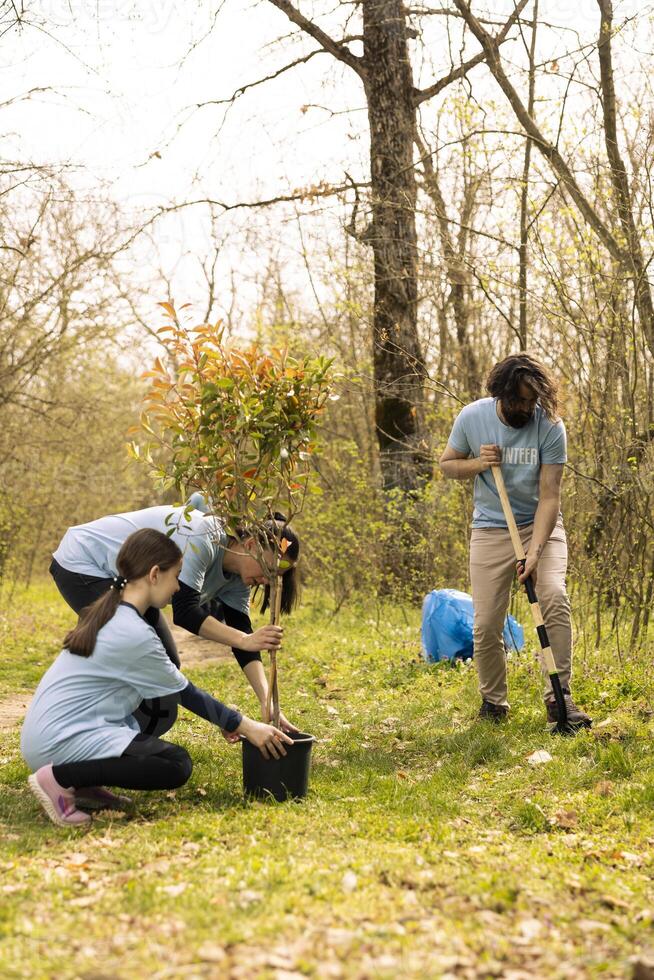 Group of activists planting small trees for nature preservation, helping with sustainability and ecosystem conservation. Volunteers joining hands for environmental care, digging holes for seeds. photo