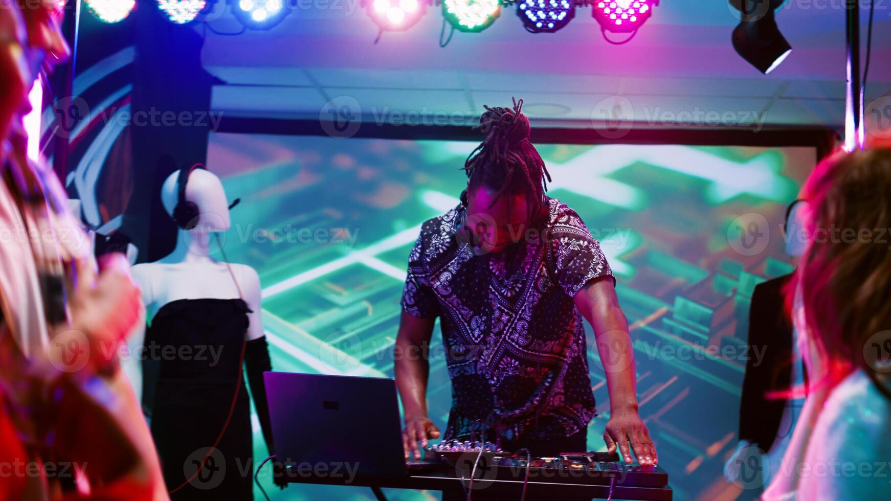 Funky adult mixing beats at club, having fun on stage audio equipment and partying. Young DJ working with sounds station dancing with people at discotheque event. Handheld shot. photo