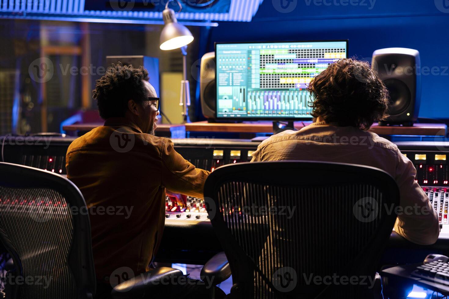 Professional sound engineer and artist working together on a new track, using digital audio software to edit and process tunes. Experts team collaborating on music, mixing at control room board. photo