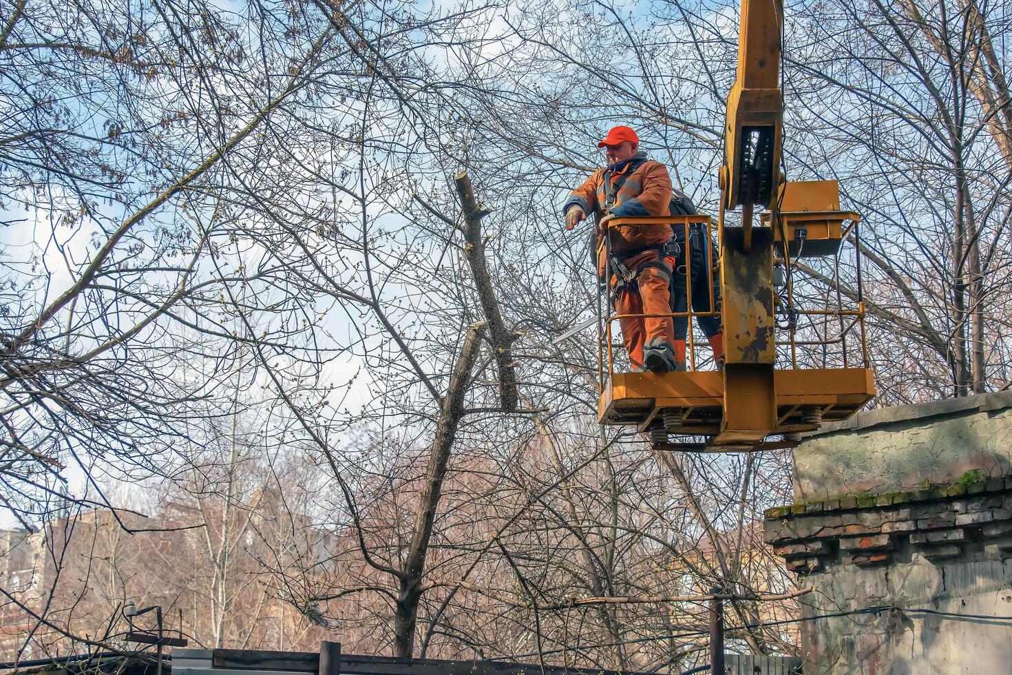 Dnepr, Ukraine - 03.20.2024 Municipal service workers stand with a chainsaw in a crane basket and trim dangerous trees photo