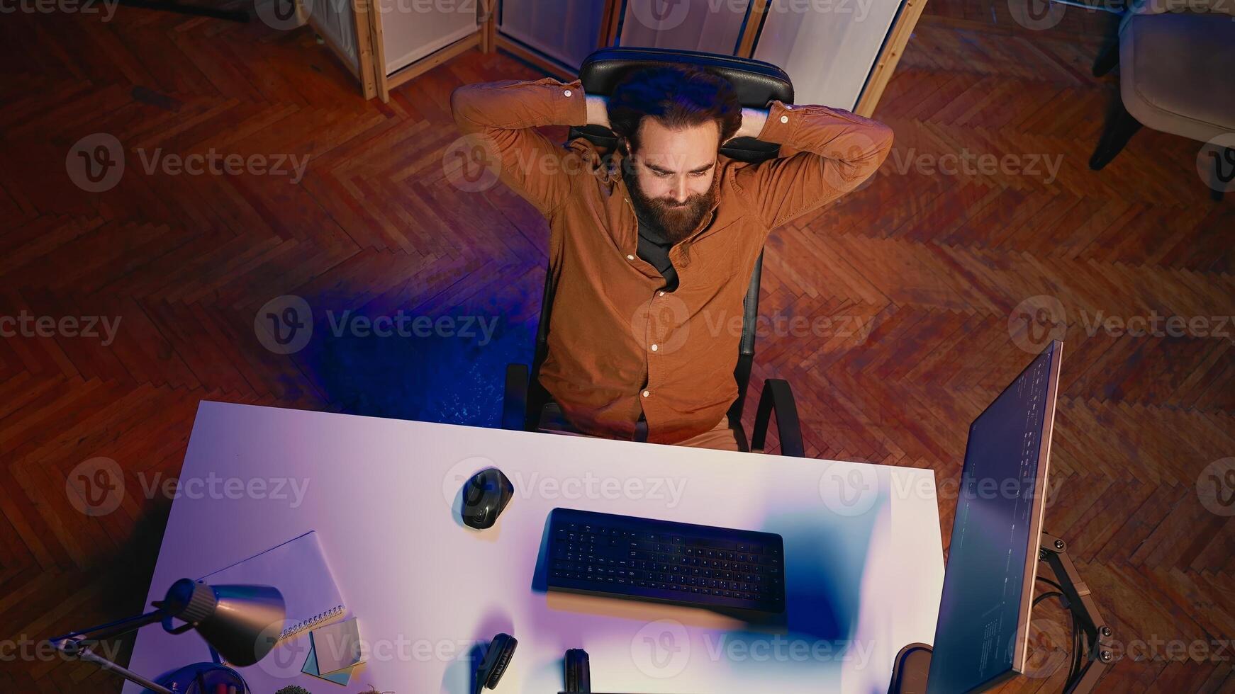 Top down view of IT admin in home office stretching after sitting on desk chair all day. Software engineer loosening up, relaxing after typing on computer for long period of time, aerial shot photo