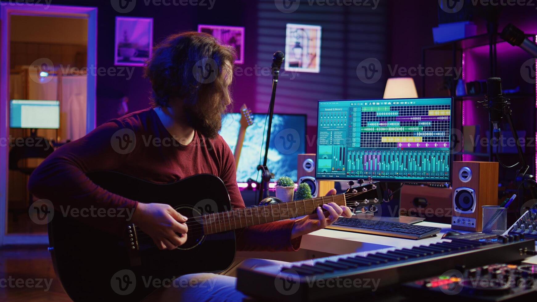 Portrait of male songwriter playing acoustic guitar and recording musical sounds to use for mix and master in home studio. Composing tunes with digital audio workstation software. Camera B. photo