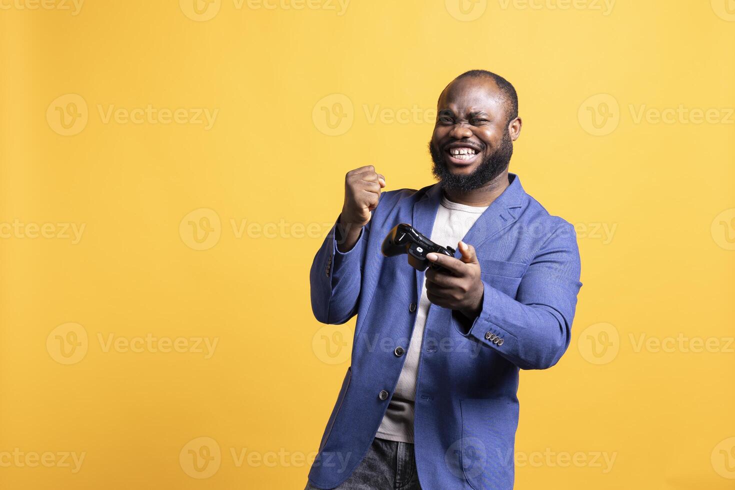 Happy BIPOC gamer celebrating after winning gaming console game, studio background. Euphoric man bragging after being victorious in game, defeating all enemies using gamepad photo