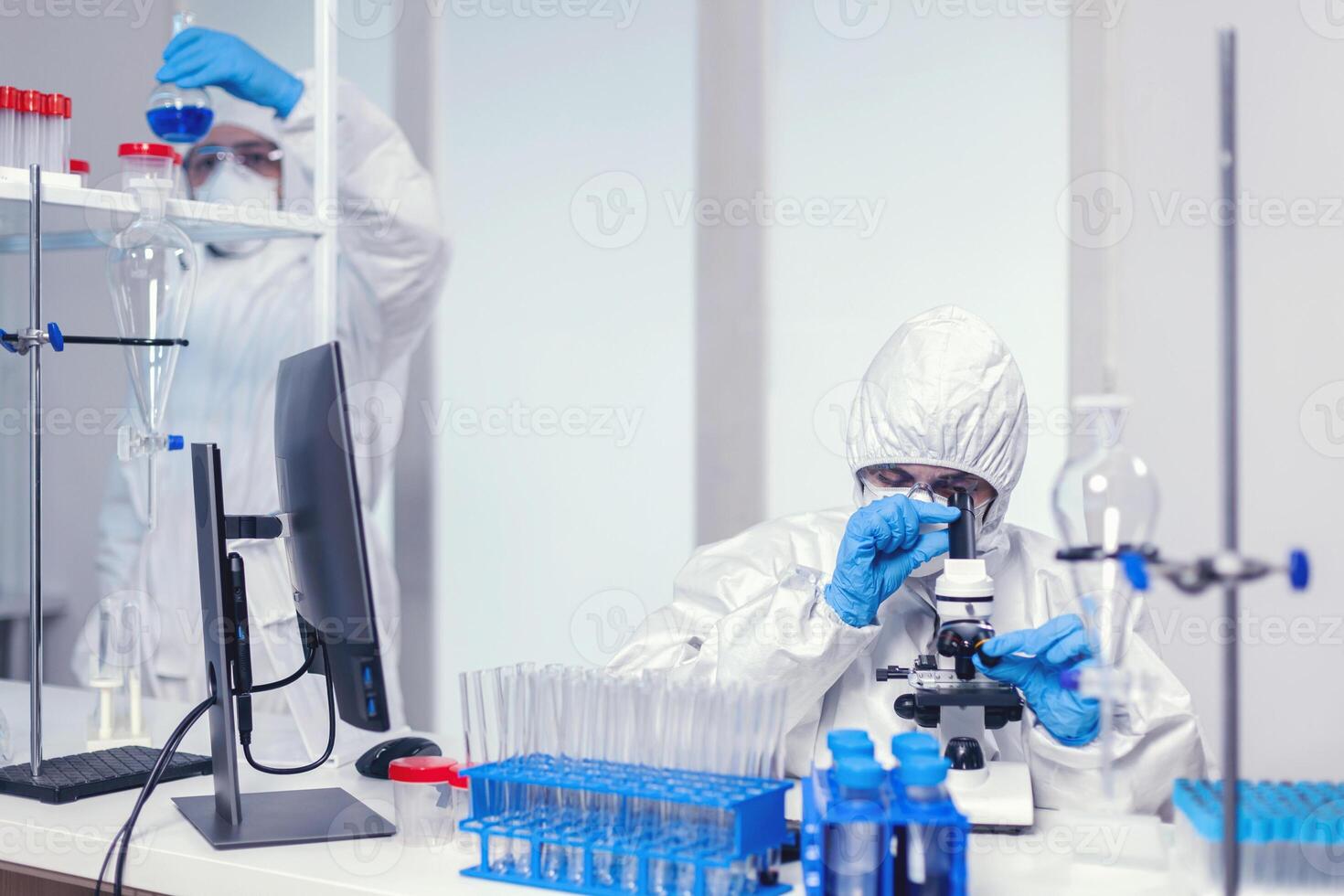 Team of medical scientist in modern laboratory searching for coronavirus vaccine wearing ppe. Chemist researcher during global pandemic with covid-19 checking sample in biochemistry lab photo