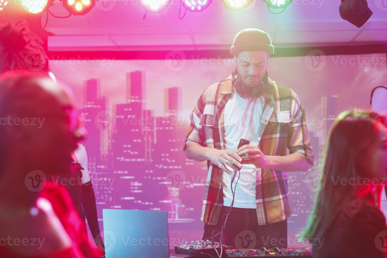 Young man musician using dj controller on stage during live concert in nightclub. Performer mixing electronic music tracks for clubbers at discotheque party in club at night photo