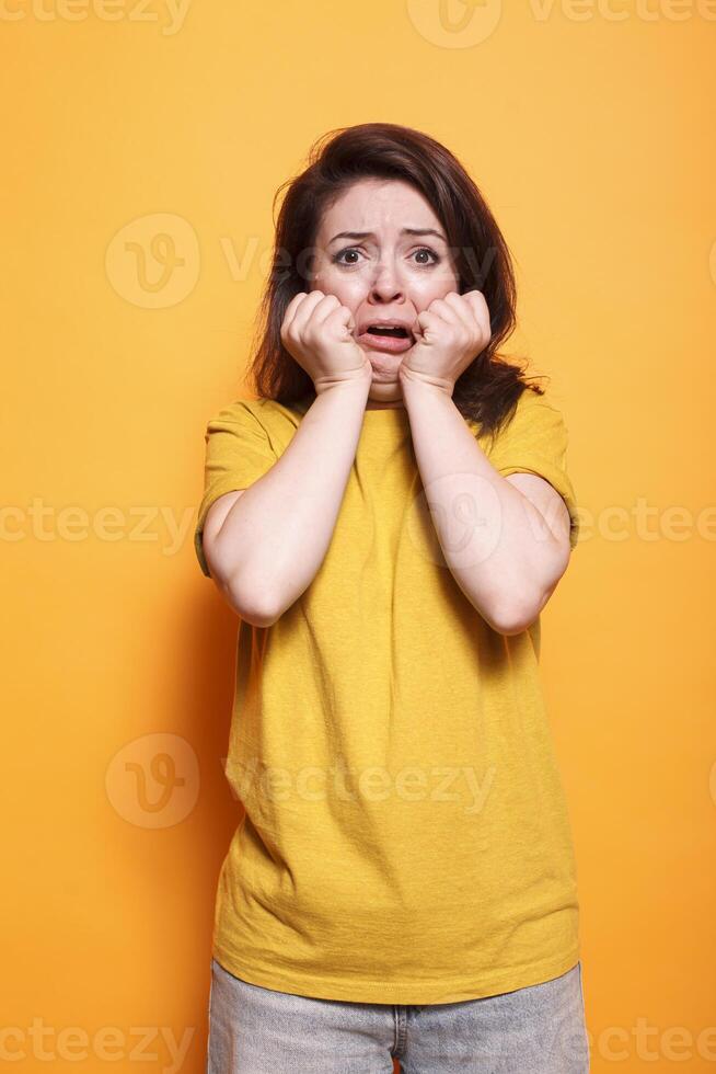 Portrait of fearful brunette lady posing for the camera with their hands on their faces. Terrified woman can be heard screaming and trembling in the studio. Emotional adult who is afraid. photo