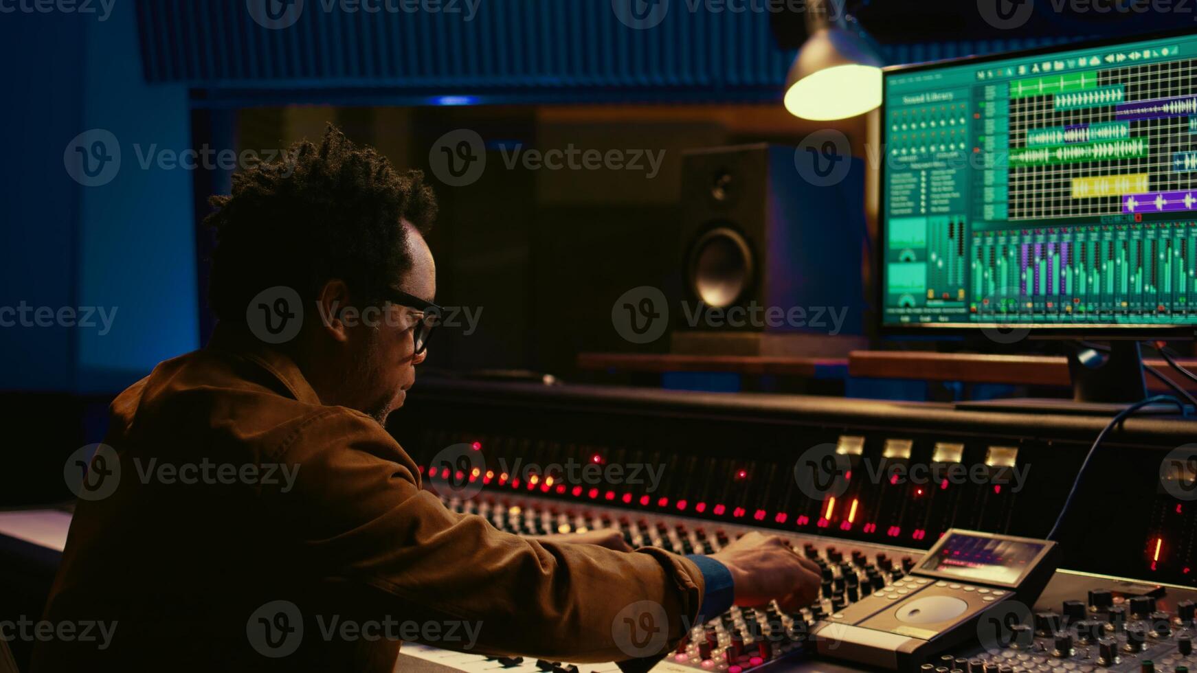 Sound designer uses mixing console and managing audio tracks, twisting knobs on control desk for adjusting tunes and volume. Producer creates music in professional studio, technical gear. Camera B. photo