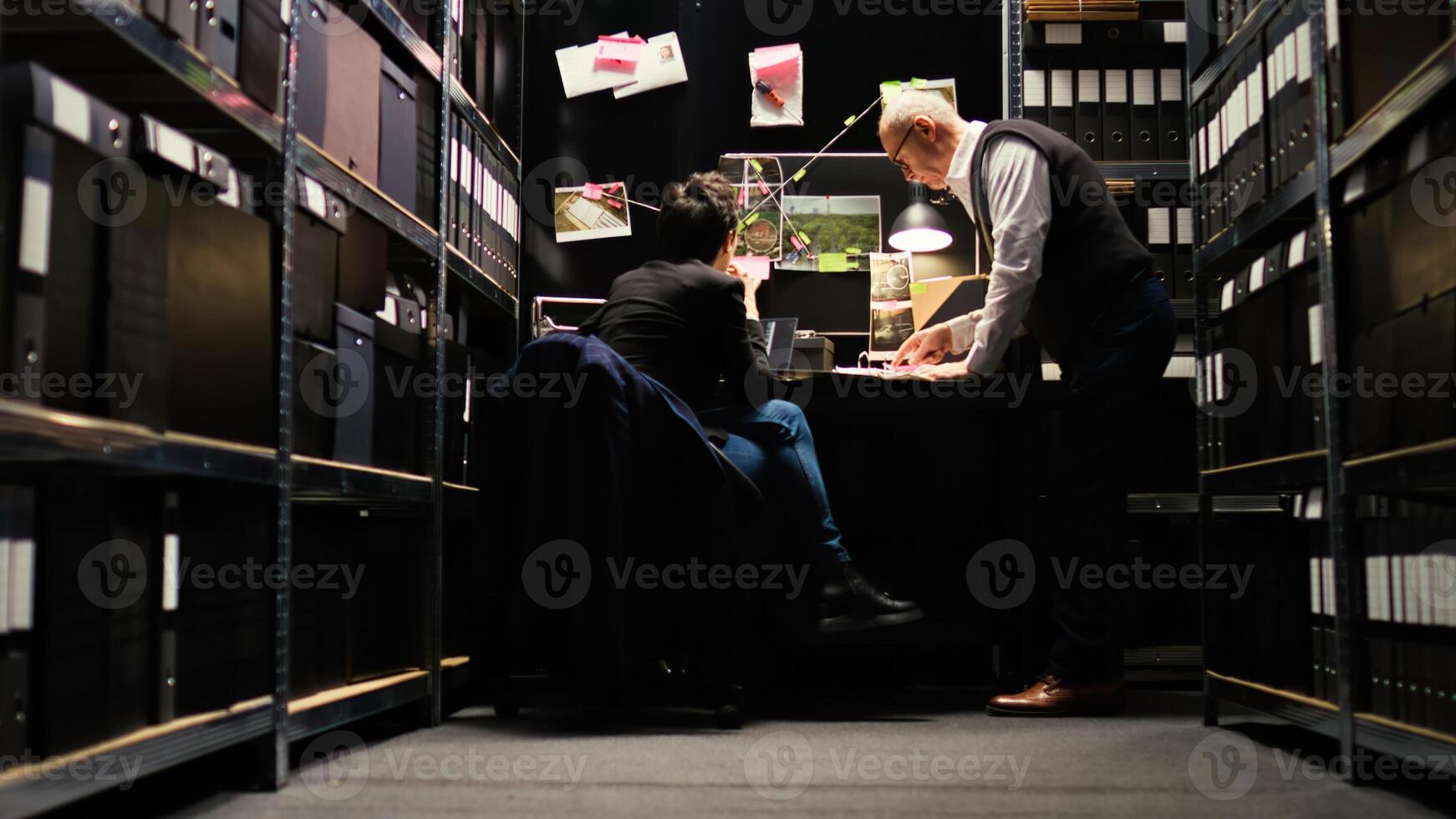 Partners work together on criminal case, inspecting classified records in police archive incident room. Team of criminologists reviewing incriminating proof before catching culprit. photo