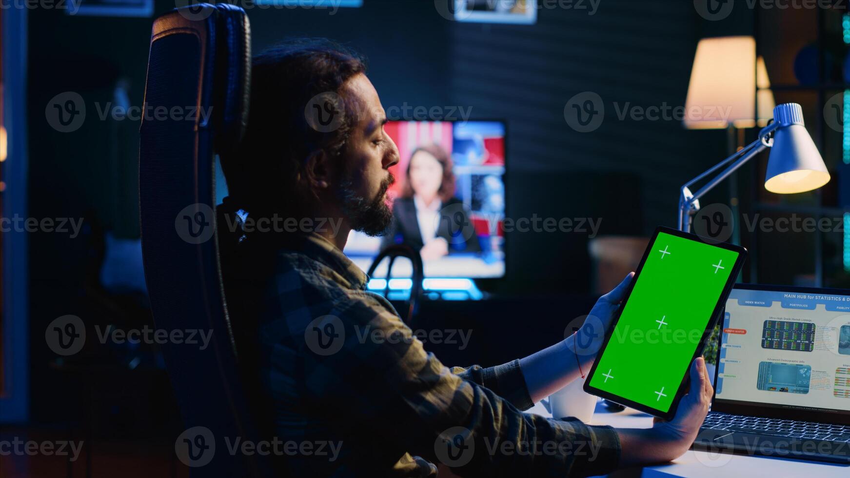 Remotely working man in home office checks statistical financial graphs on laptop, crosschecking with data on chroma key tablet. Freelancer holding isolated screen device, analyzing business graphics photo