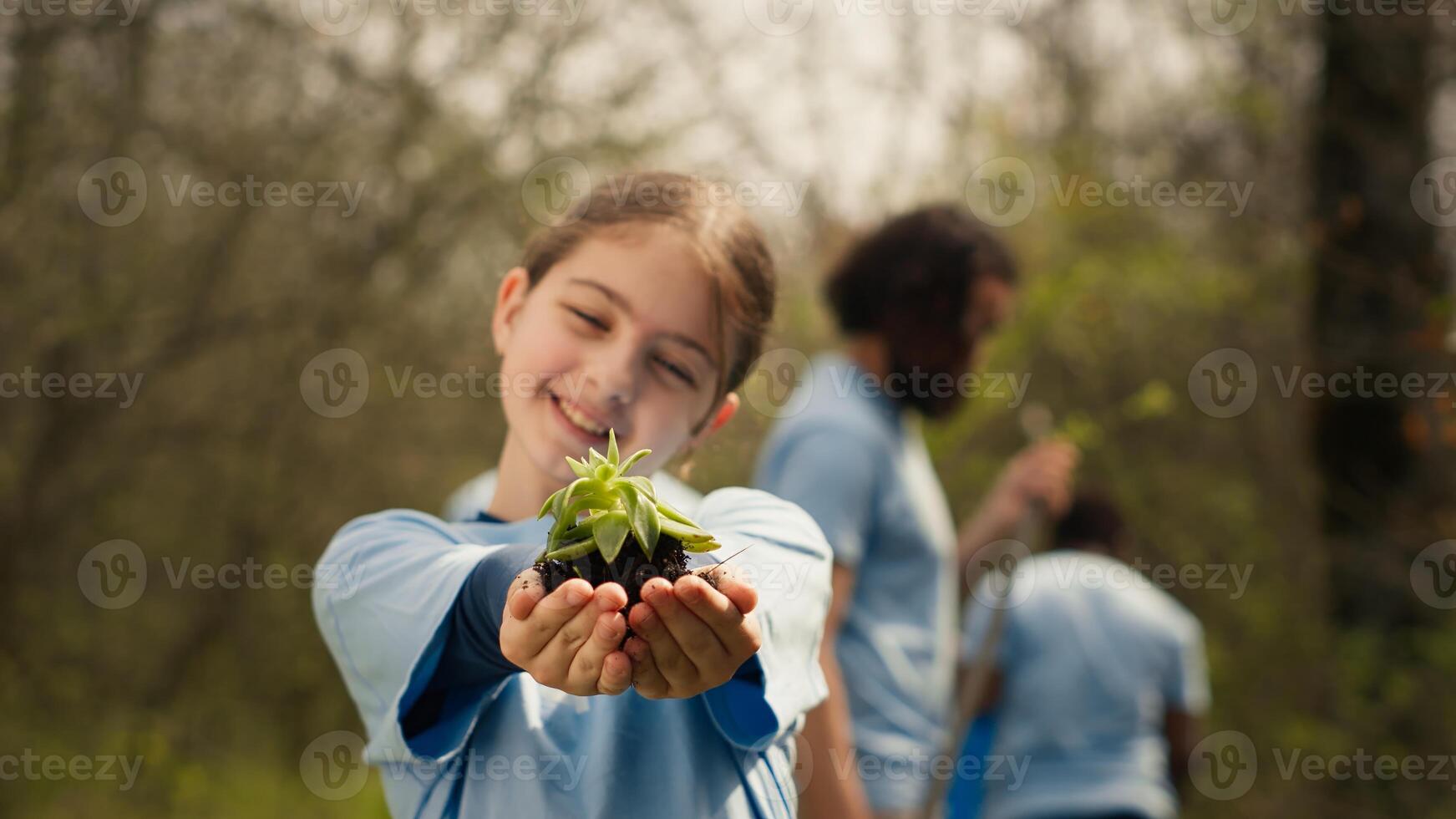 Little kid volunteer holding a small seedling with natural soil in hands, presenting plant for new habitat in the forest. Child fighting nature preservation, environmental care awareness. Camera A. photo