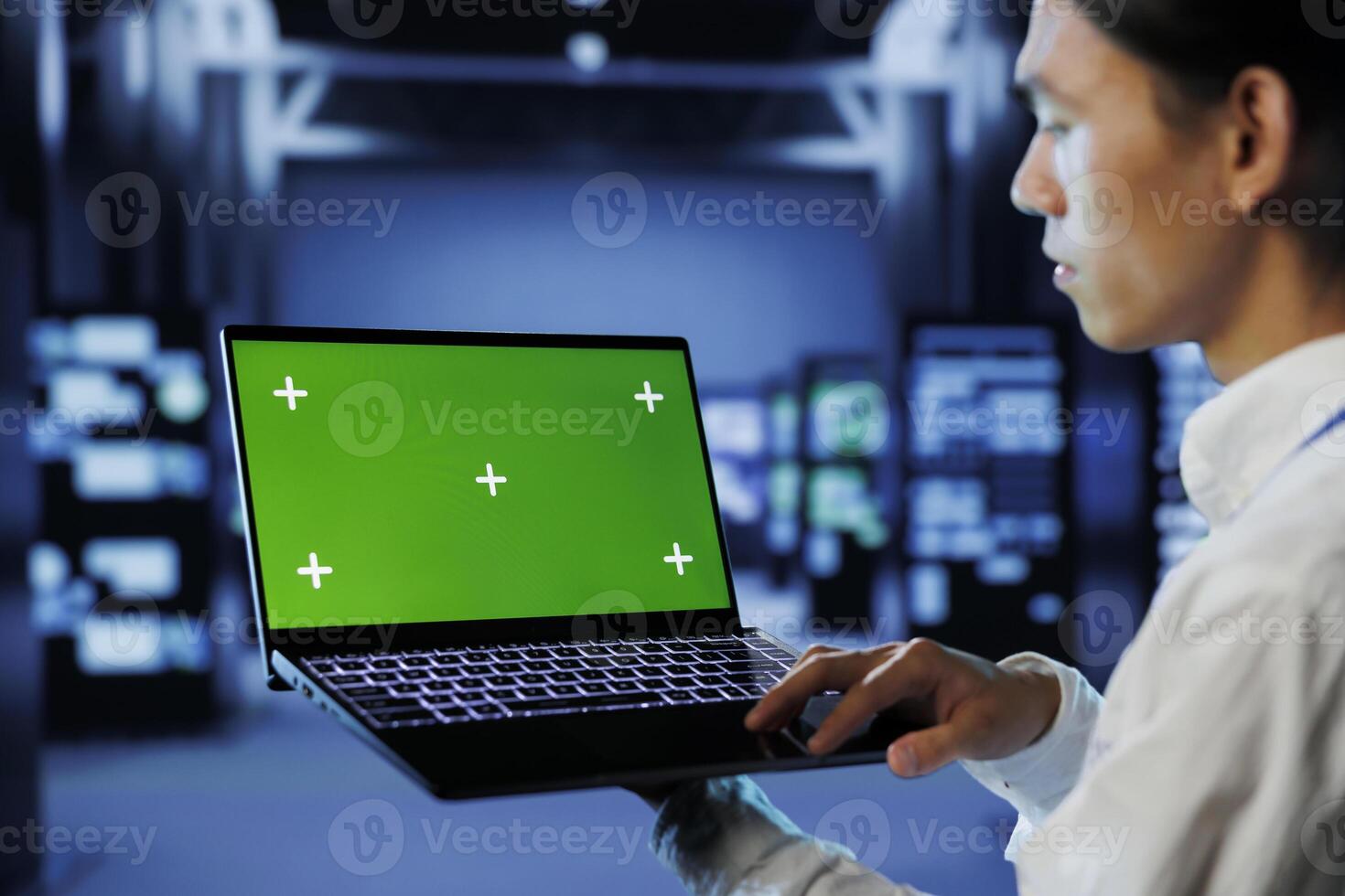IT consultant with green screen laptop between server hub clusters providing processing resources for businesses worldwide. Worker uses mockup device to fix data center mainframes photo