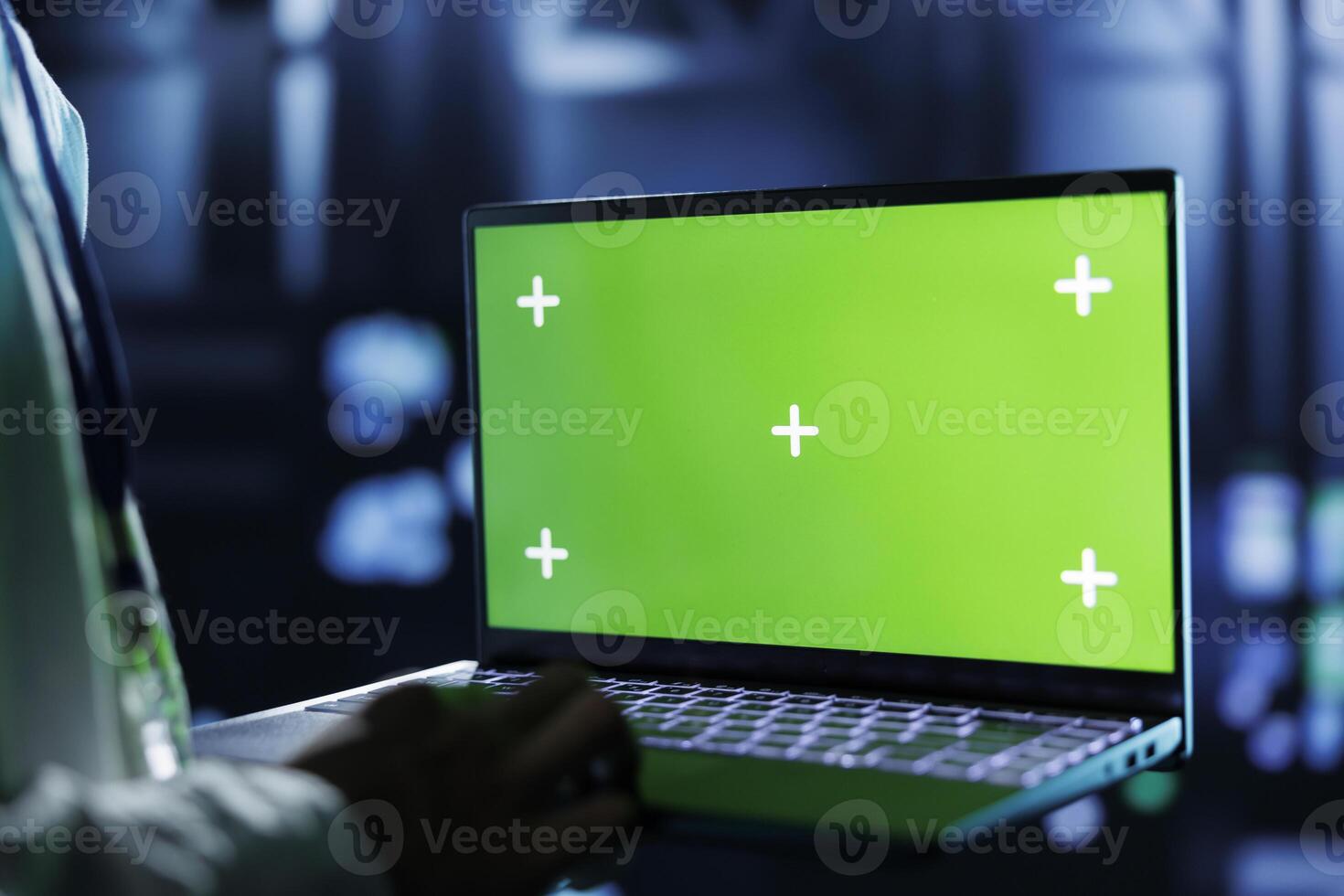 Dara center system administrator running code and programming on green screen laptop, troubleshooting and upgrading high tech establishment designed to accommodate rows of fully operational servers photo