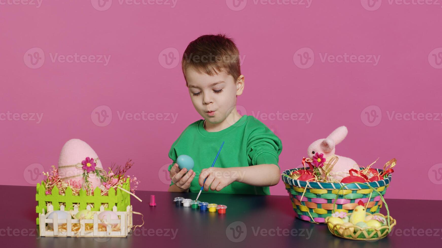 Joyful small kid painting eggs for easter holiday festivity in studio, using watercolor and art supplies. Smiling preschooler coloring festive ornaments in preparation for sunday. Camera A. photo