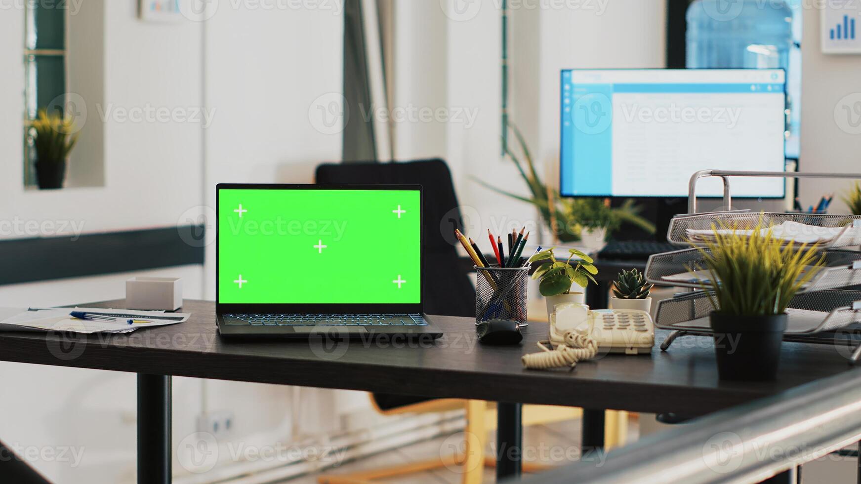 Office with green screen laptop and display in background with scheduled clients list. Mockup notebook in workspace and customers financial consultations list in the back on monitor photo