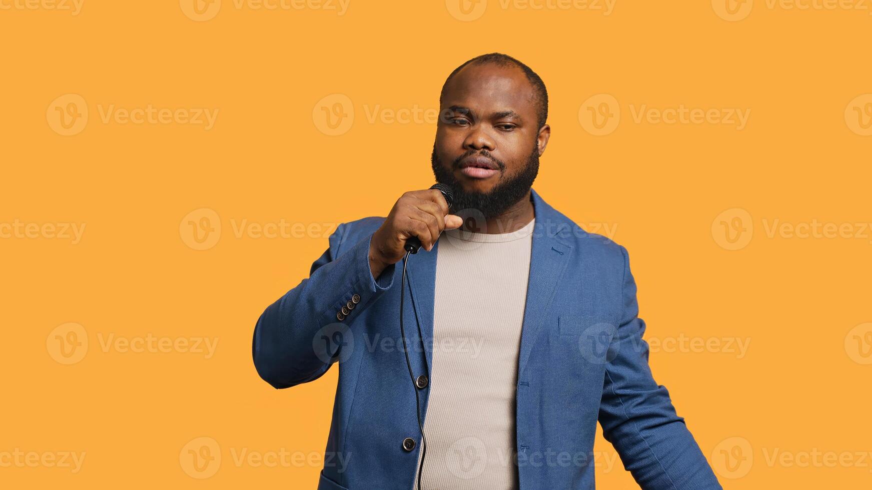 Smiling singer holding microphone, performing tunes during concert isolated over yellow studio background. Merry musician singing to imaginary crowd, performing on scene, camera A photo