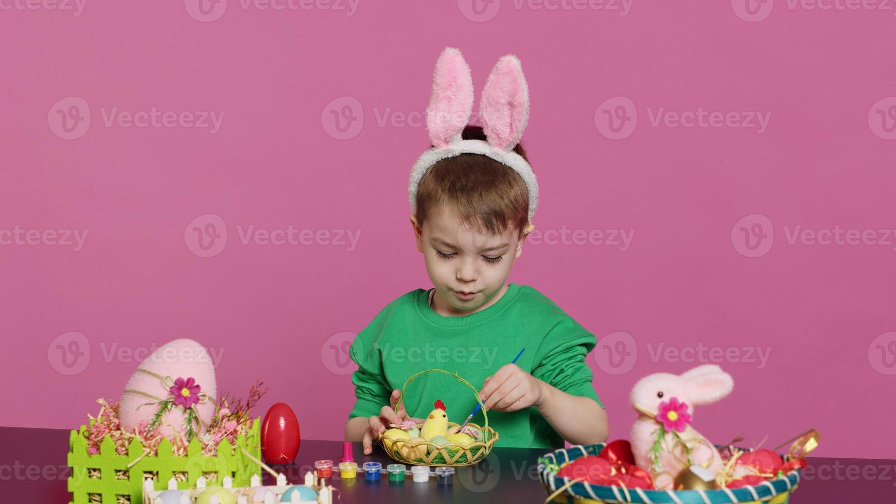 Happy small child arranging eggs and chick in a basket in preparation for easter sunday celebrations, creating festive decorations in studio. Little boy having fun coloring. Camera A. photo