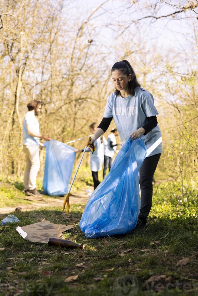 Woman environmentalist collecting junk from the ground to combat pollution within the forest ecosystem, environmental care. Activist doing community service to clean the woods from trash. photo
