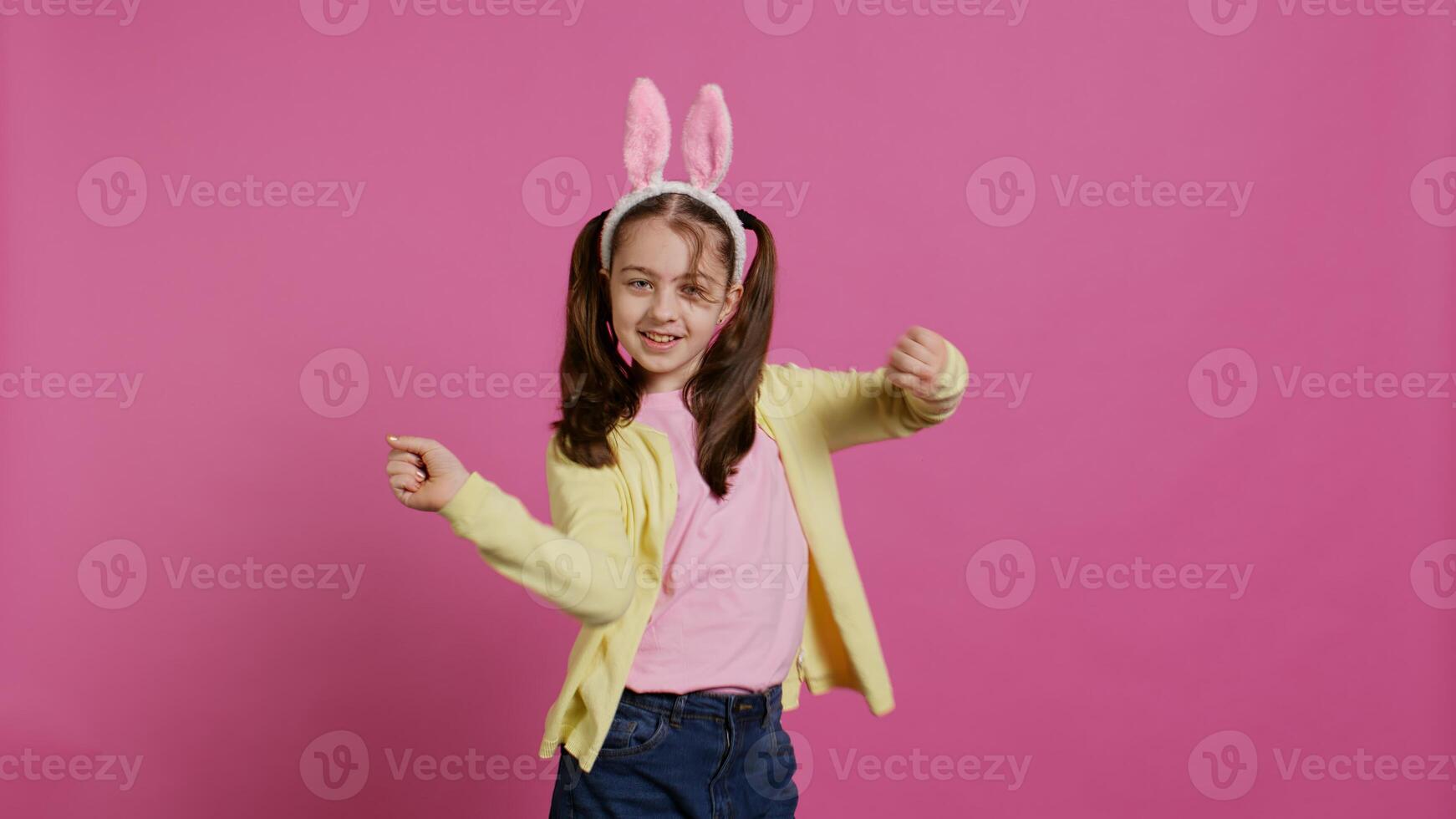 Confident cheery girl showing dance moves in the studio, feeling cheerful and positive about easter holiday festivity. Talented child dancing around and wearing bunny ears. Camera B. photo