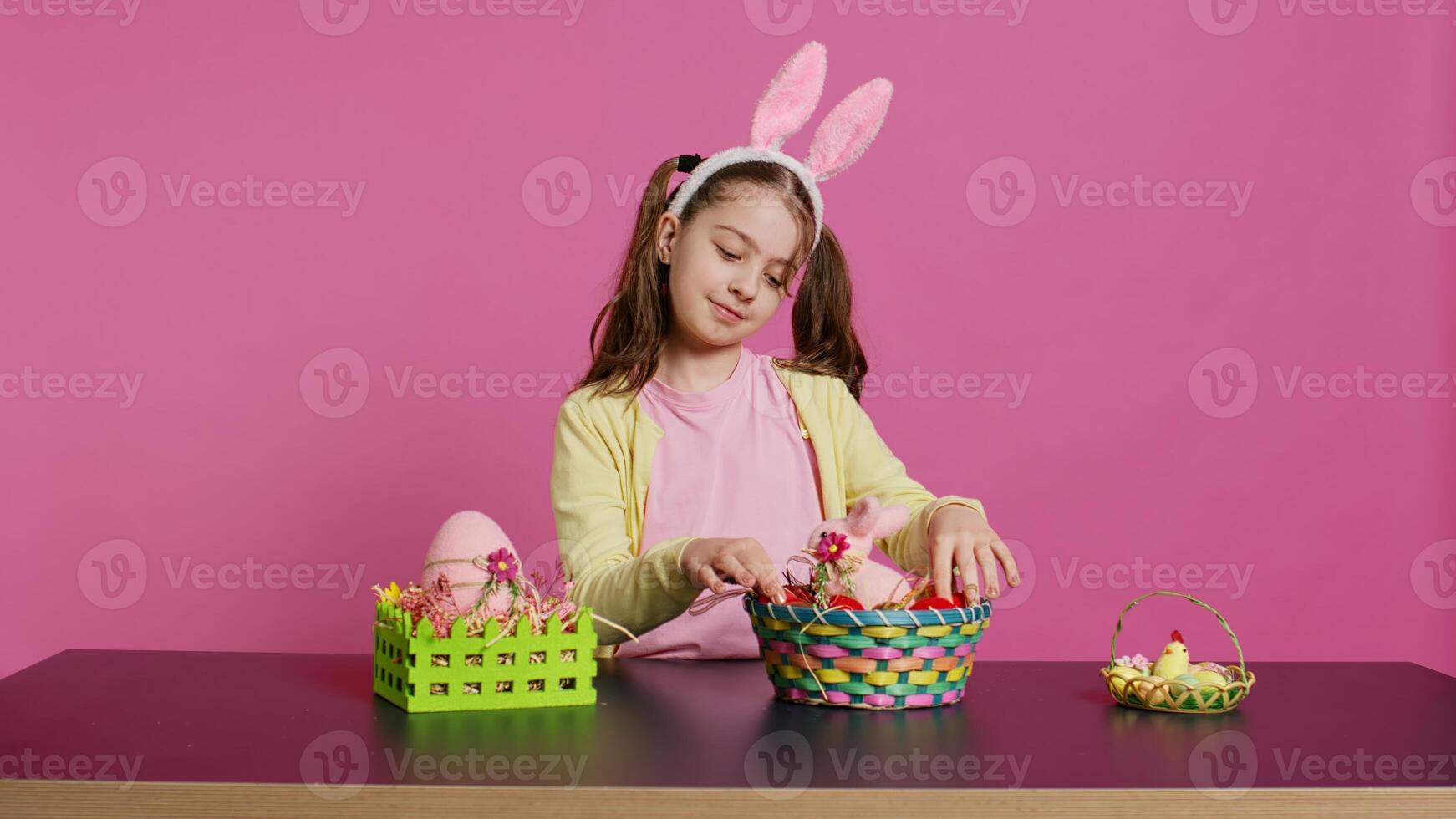 emocionado joven niña arreglando pintado huevos en un cesta a preparar para Pascua de Resurrección fiesta celebracion, creando festivo preparativos. juguetón contento niñito con conejito orejas, creativo actividad. cámara b. foto