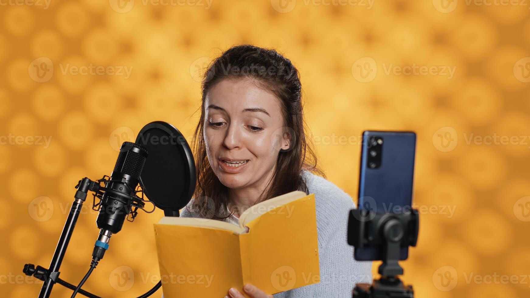 Media star filming vlog at work, reading book to record audiobook, studio background. Voice actor doing content creation while producing digital recording on novel using microphone, camera A photo