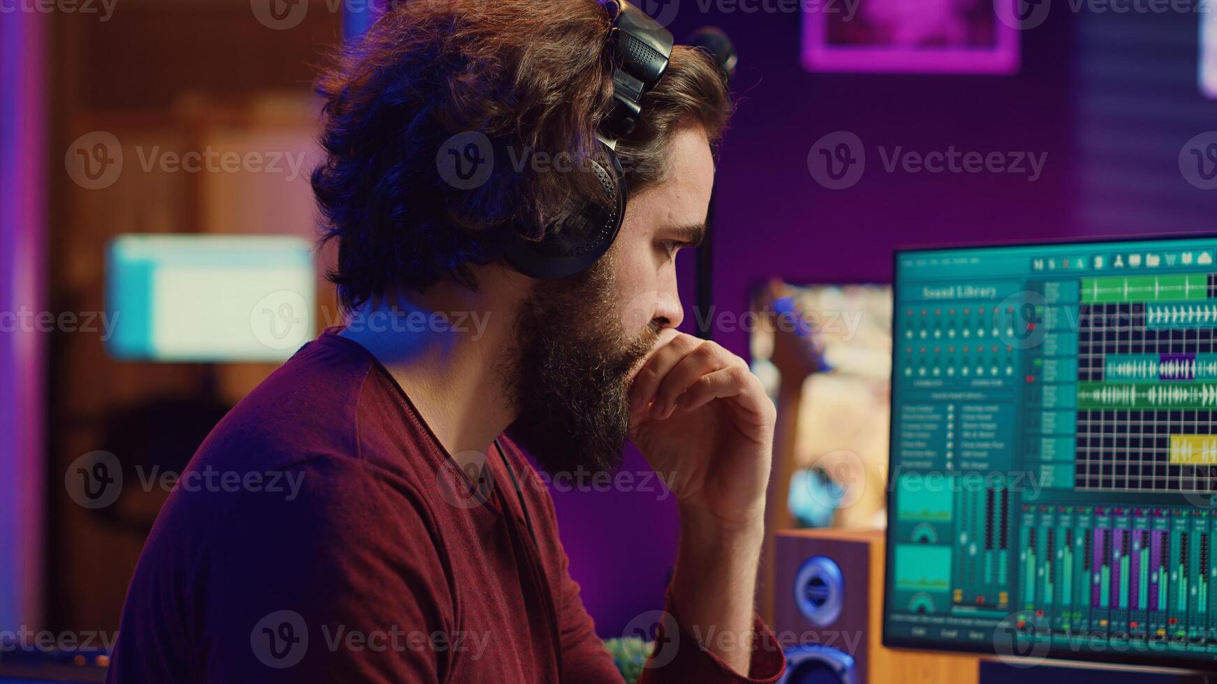 Music producer engages in post production with editing and time aligning recorded songs. Musician using digital audio workstations to manipulate tunes, adding audio effects. Camera A. photo