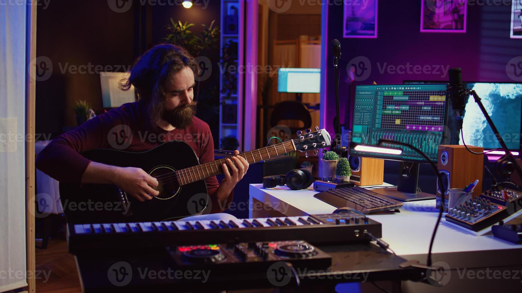 Music producer tuning his acoustic guitar before playing instrument, recording and mixing tunes to create new soundtracks. Singer composing a song using electronic panel controls. Camera B. photo