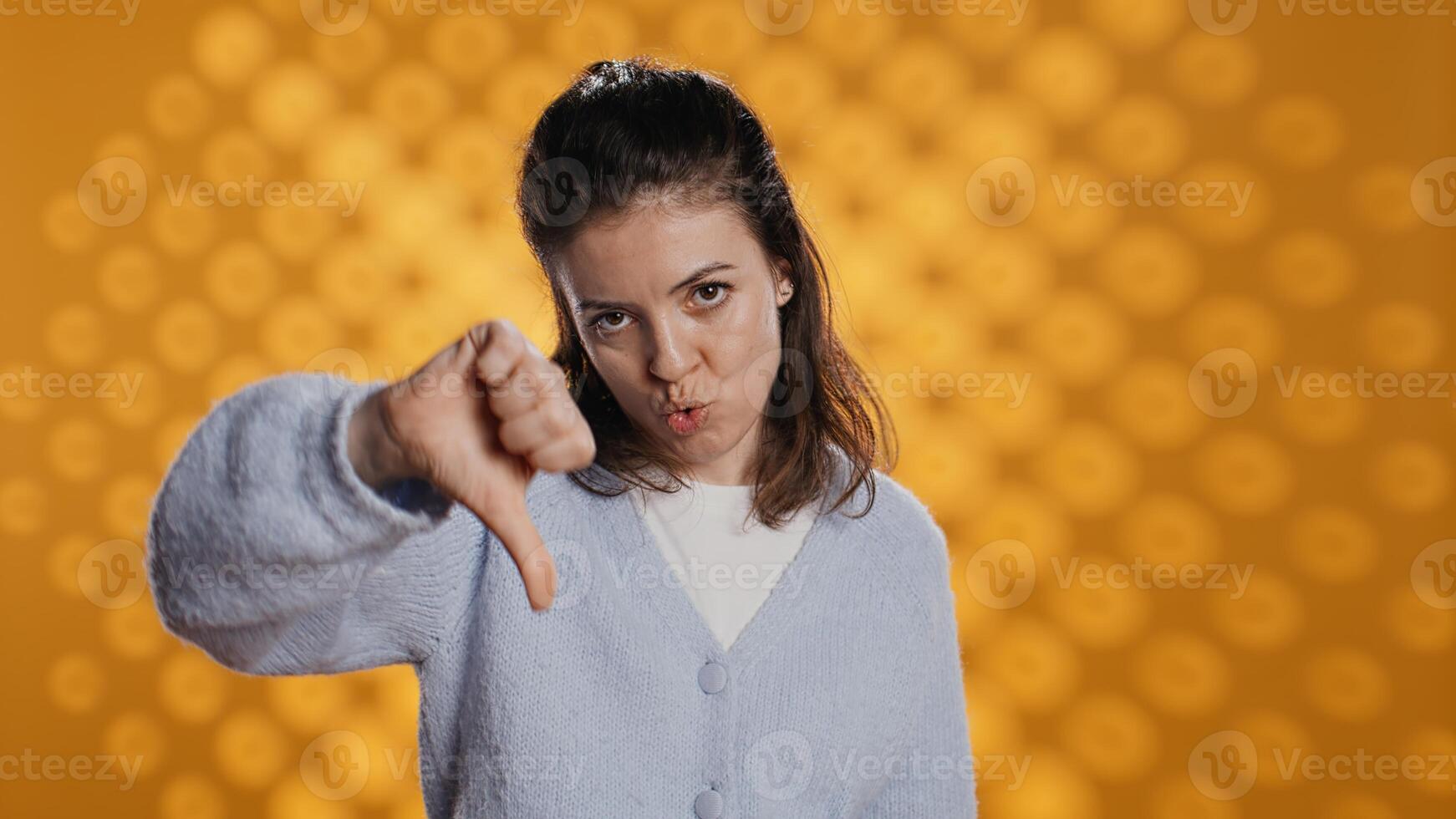 Disappointed woman bashing book, showing thumbs down hand sign, isolated over studio background. Upset bookworm dissatisfied with new novel, giving negative review, camera B photo