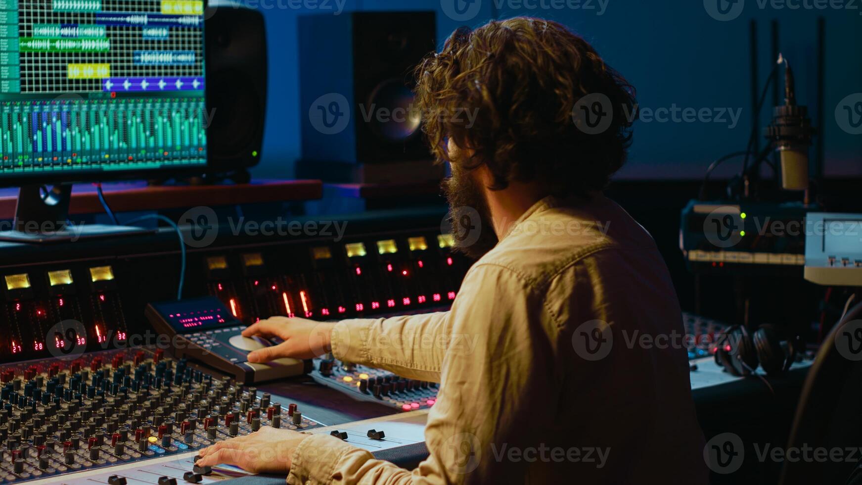 Music producer editing tracks with mixing console and audio software in studio, pressing key buttons and twisting knobs in control room. Sound engineer producing tunes and adjusting volume. Camera A. photo